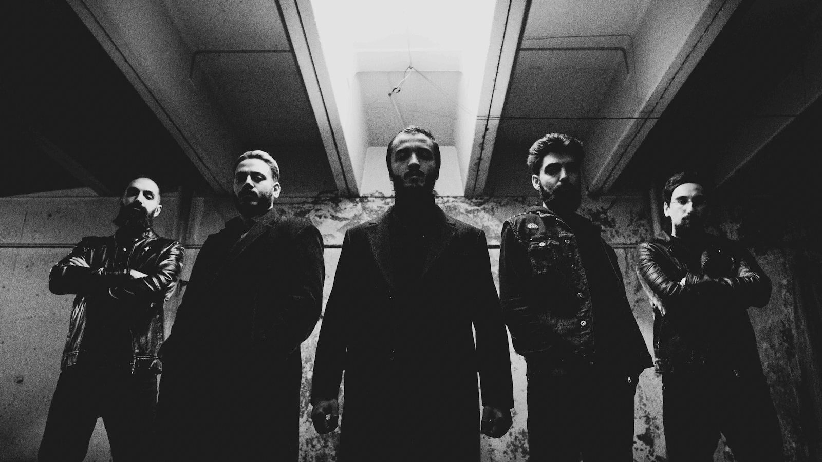 grayscale photo of 3 men in black suit standing in front of the wall
